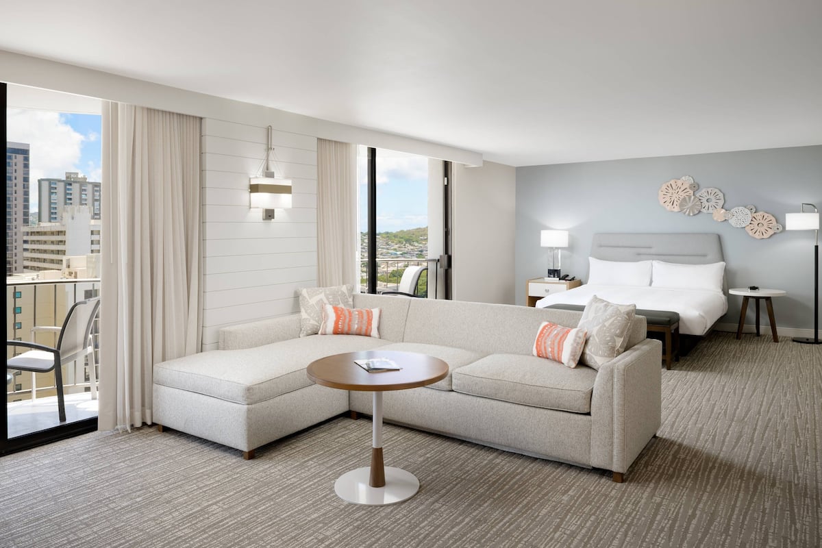 Ein modernes Hotelzimmer mit einem großen Bett, einer Sitzecke, einem kleinen runden Tisch und Blick auf die Stadt.