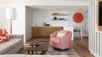 A modern living room with a sofa, a pink armchair, a wooden coffee table, and a kitchen in the background.
