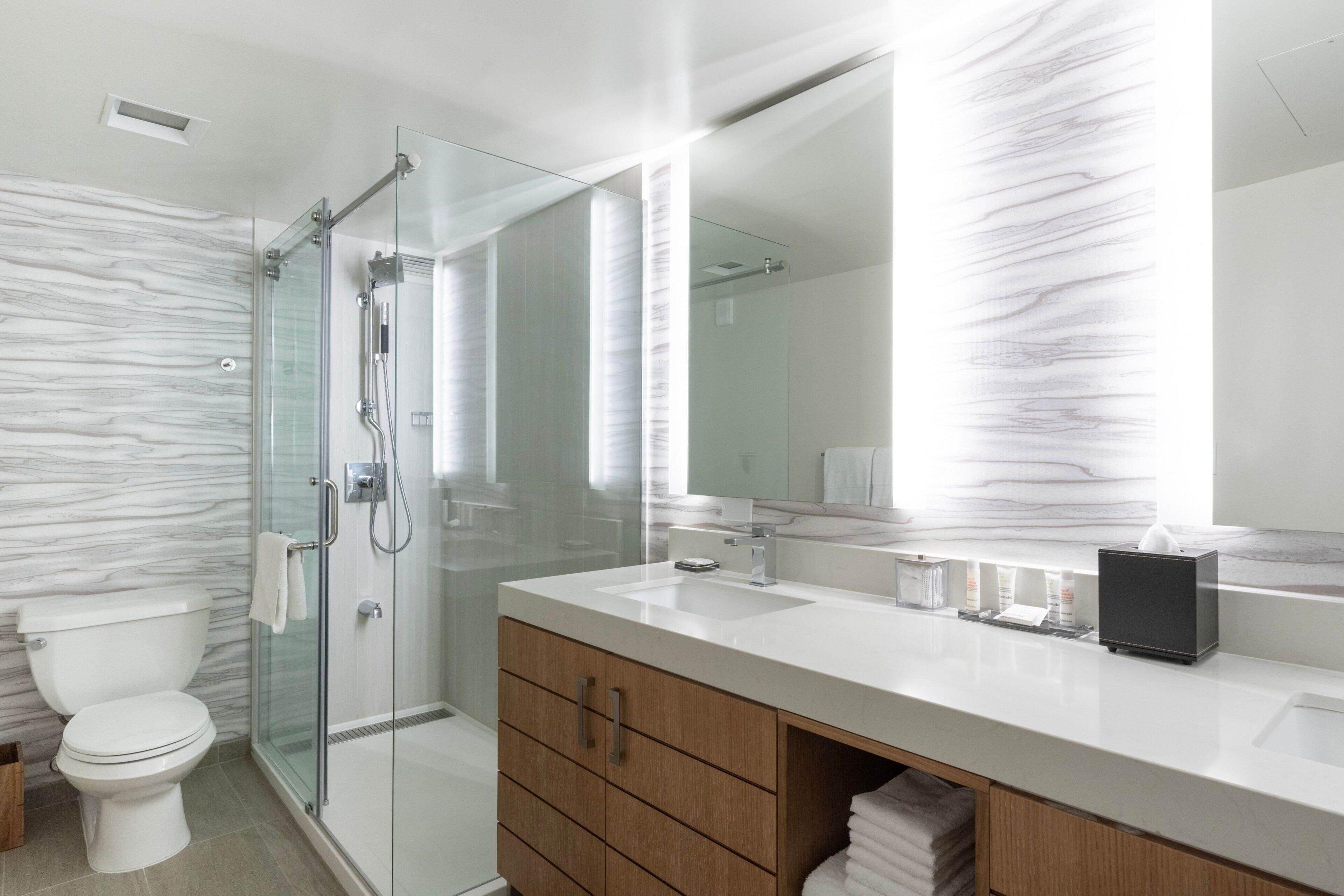 A modern bathroom with a glass shower enclosure, a white toilet, and a wooden vanity with a mirror above it.