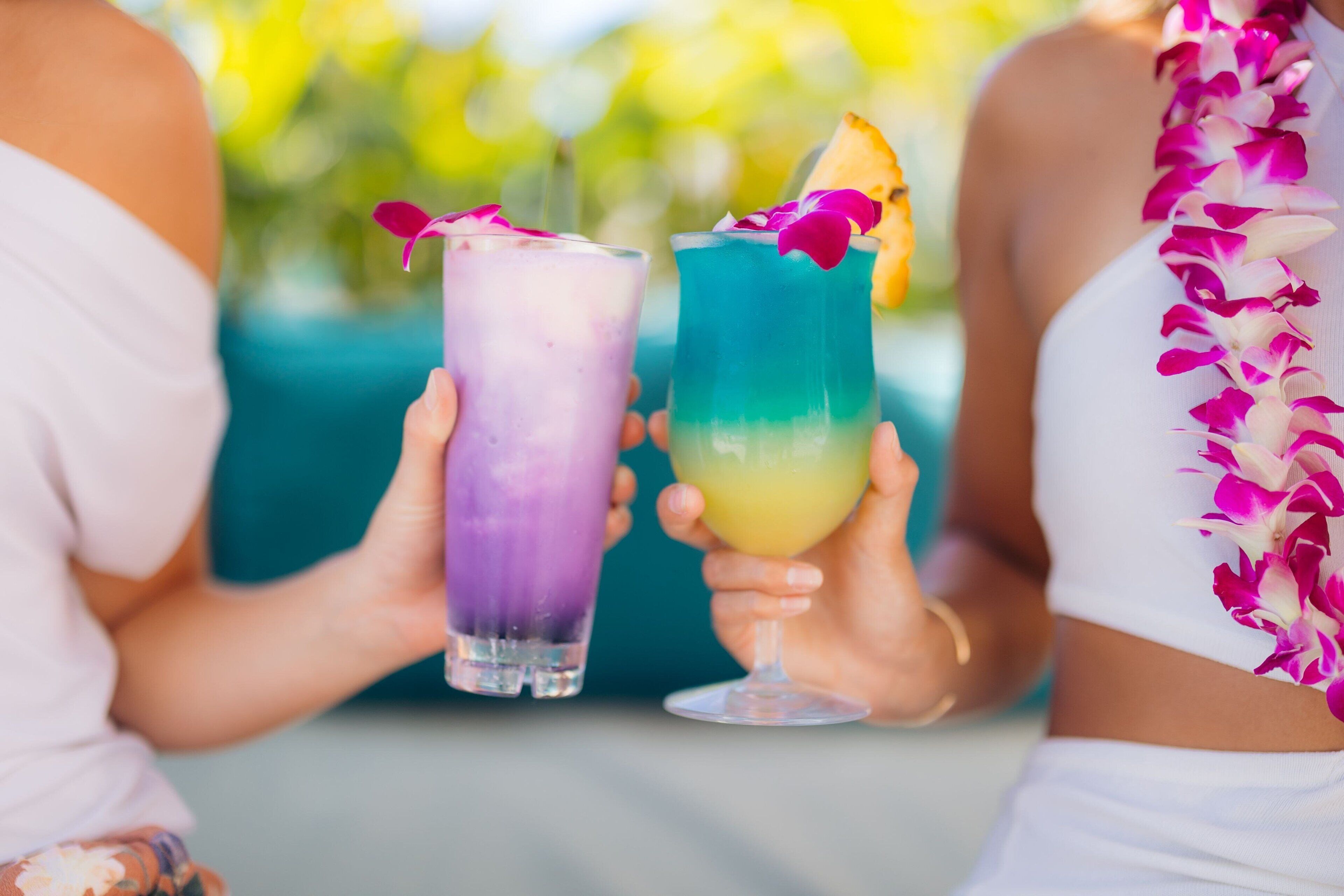 Two people holding colorful drinks with flower garnishes.