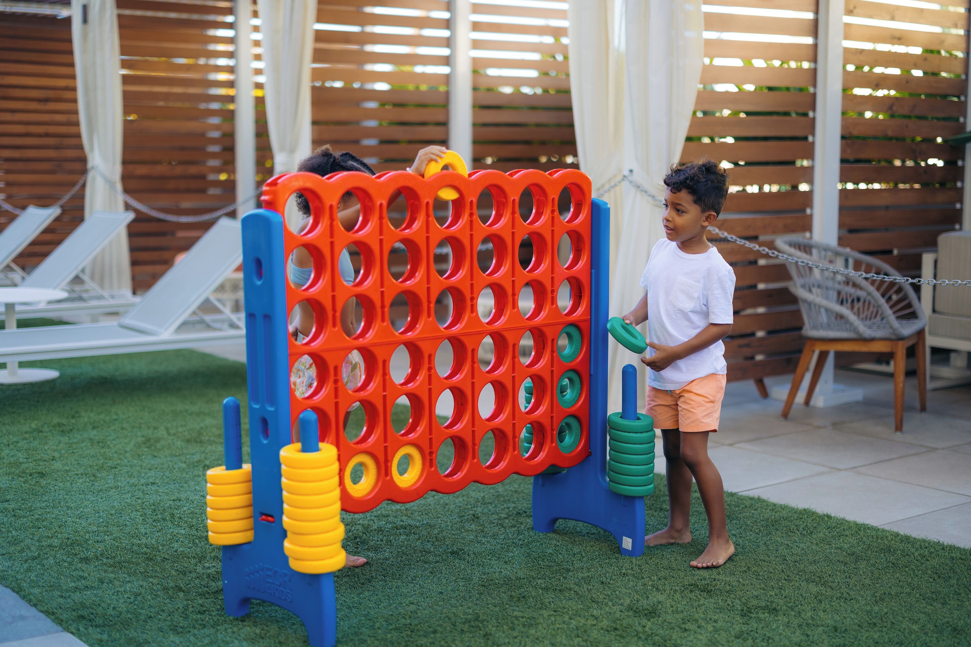 A child playing with a colorful toy structure in a backyard with artificial grass and a wooden fence.