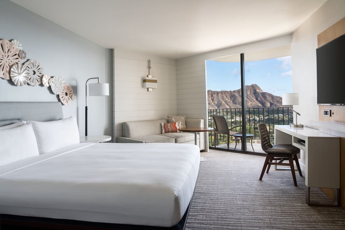 Ein Hotelzimmer mit einem großen Bett, einem Schreibtisch und einem Balkon mit Blick auf die Berge.