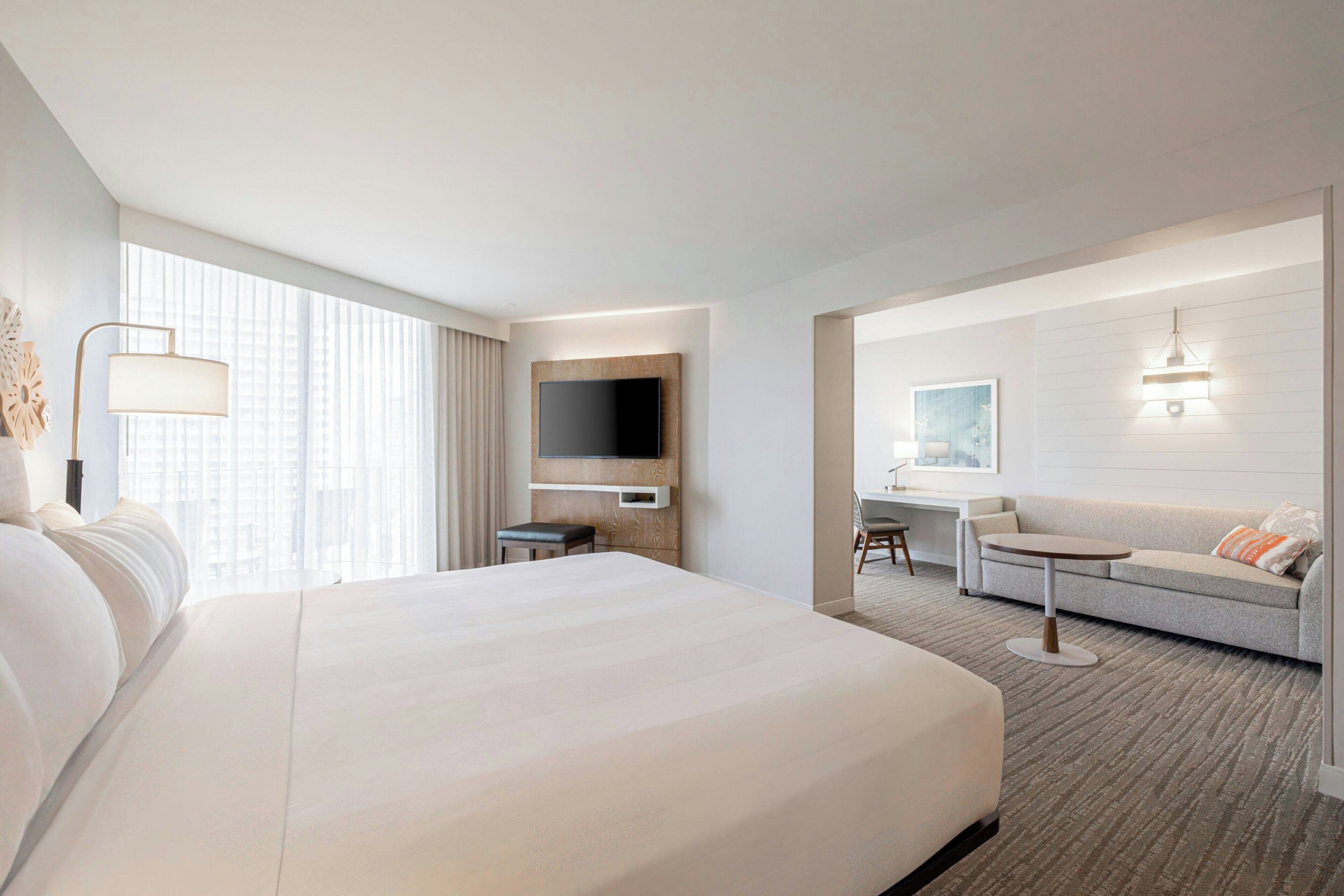 A hotel room with a large bed, a desk, a sofa, a television, and a window with curtains.