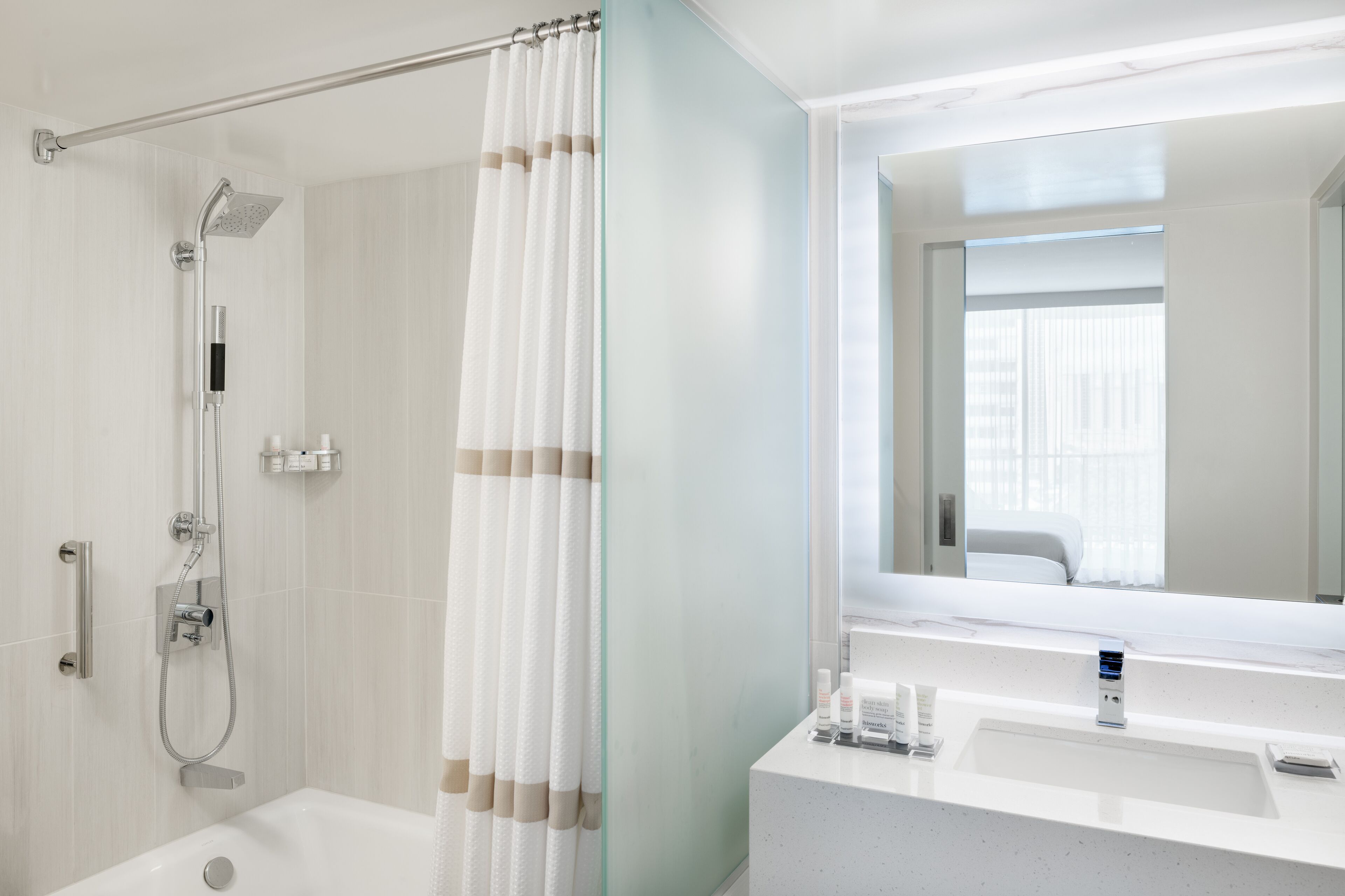 Un baño moderno con cabina de ducha de vidrio, bañera, tocador con espejo y ventana que proporciona luz natural.