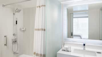 Un baño moderno con cabina de ducha de vidrio, bañera, tocador con espejo y ventana que proporciona luz natural.
