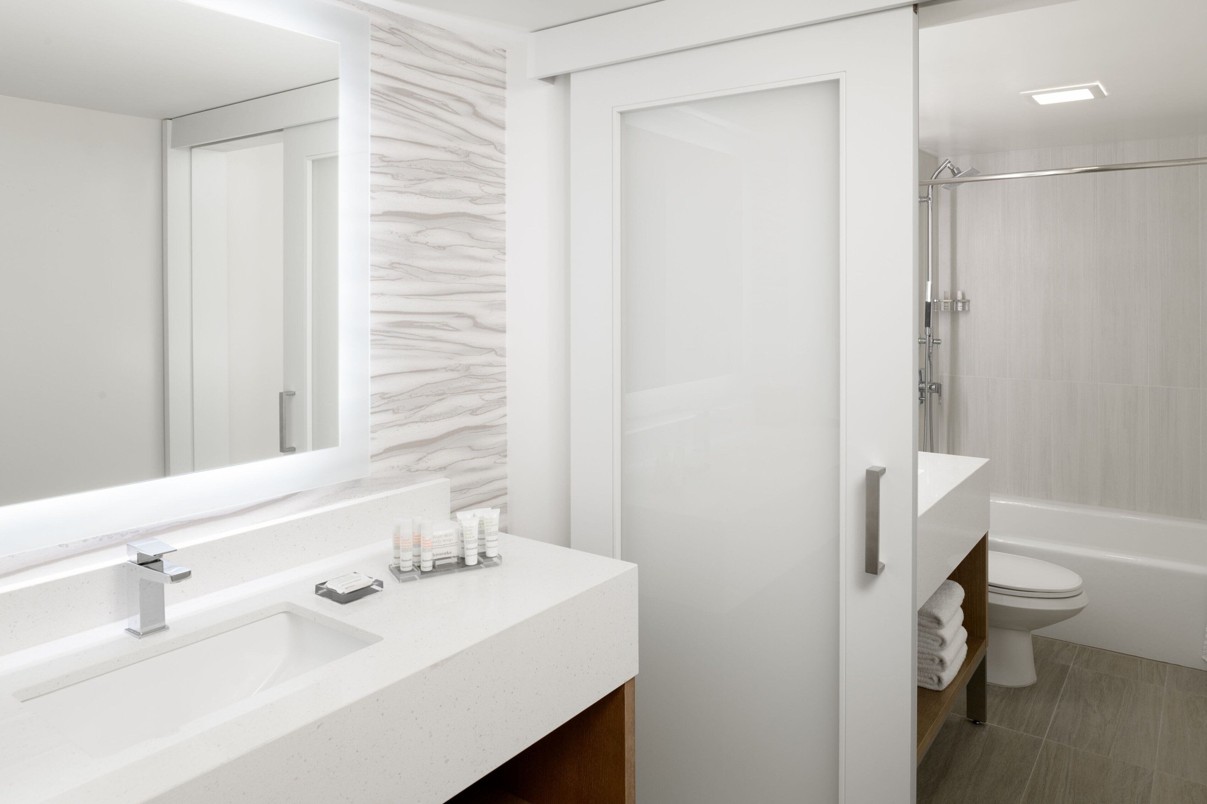 Un baño moderno con tocador blanco, un espejo grande y zona de ducha.
