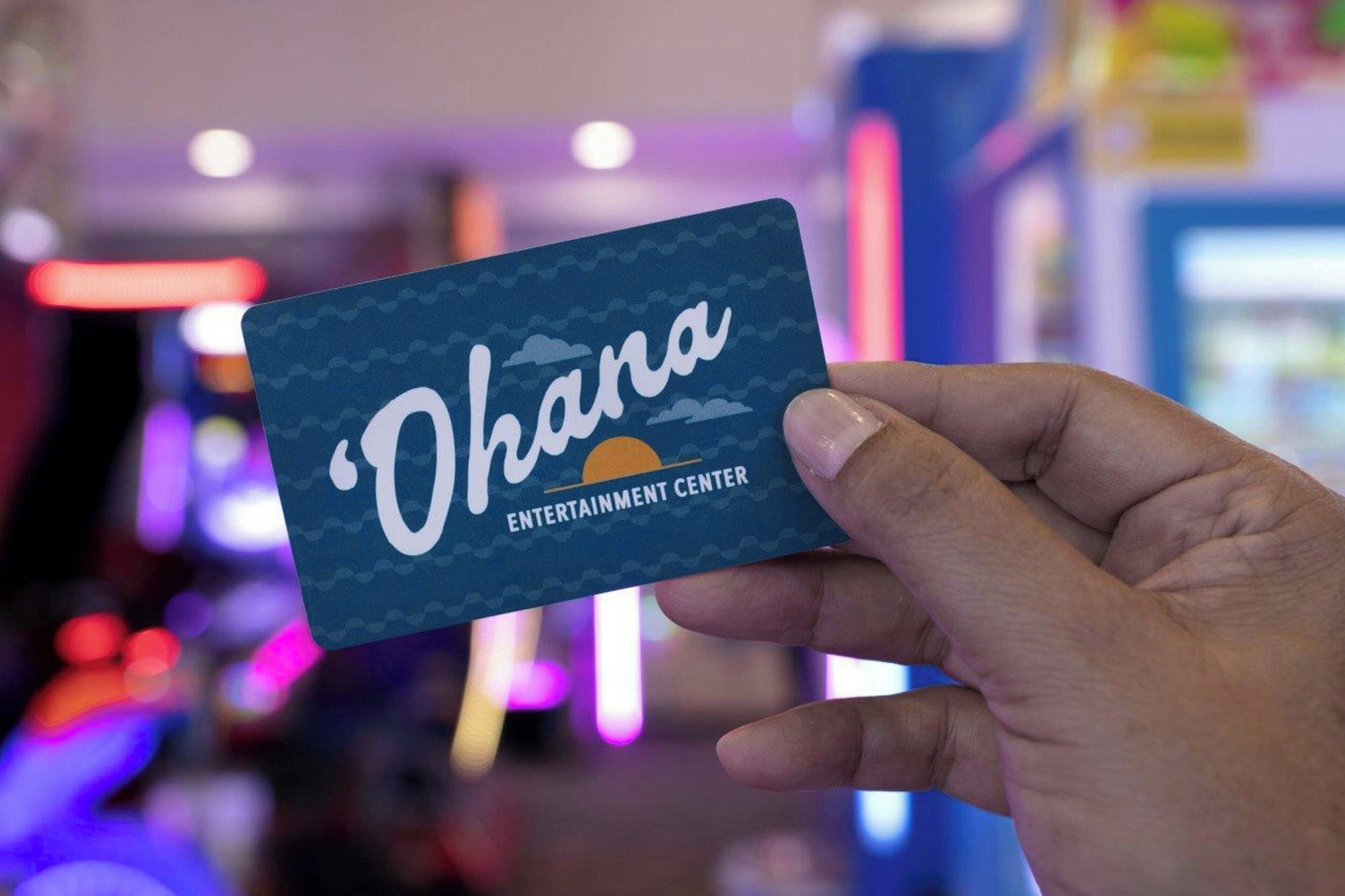 Una mano che tiene un cartello con la scritta 'Ohana Entertainment Center' su uno sfondo sfocato con luci colorate.