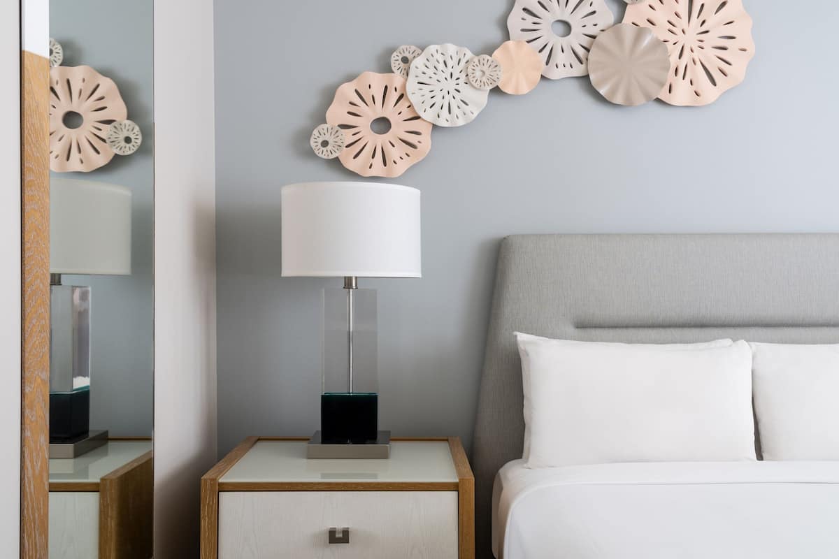 Ein ordentlich eingerichtetes Schlafzimmer mit einem Bett, einem Nachttisch mit Lampe und einer Wanddekoration.