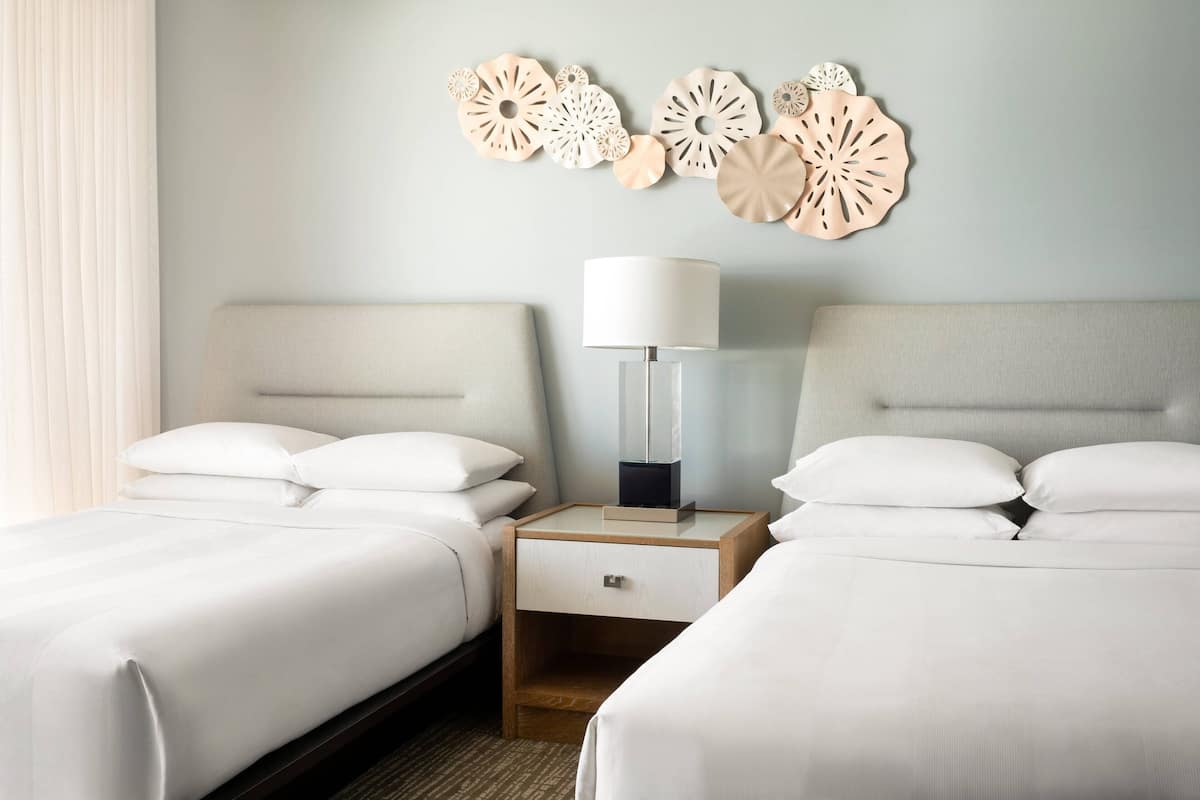 Ein Hotelzimmer mit zwei Betten, einem Nachttisch mit Lampe und dekorativen Wandbildern.