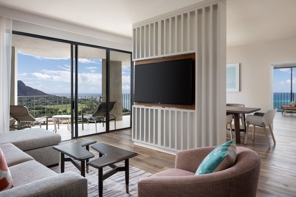 Ein modernes Wohnzimmer mit großem Flachbildfernseher, bequemen Sitzgelegenheiten und einem Balkon mit schöner Aussicht.