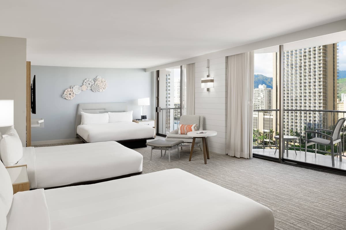 Ein Hotelzimmer mit zwei Betten, einem kleinen Tisch, einem Sessel und einem Balkon mit Blick auf hohe Gebäude.