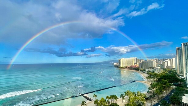 Paisagem costeira com céu claro, um arco-íris e uma praia.