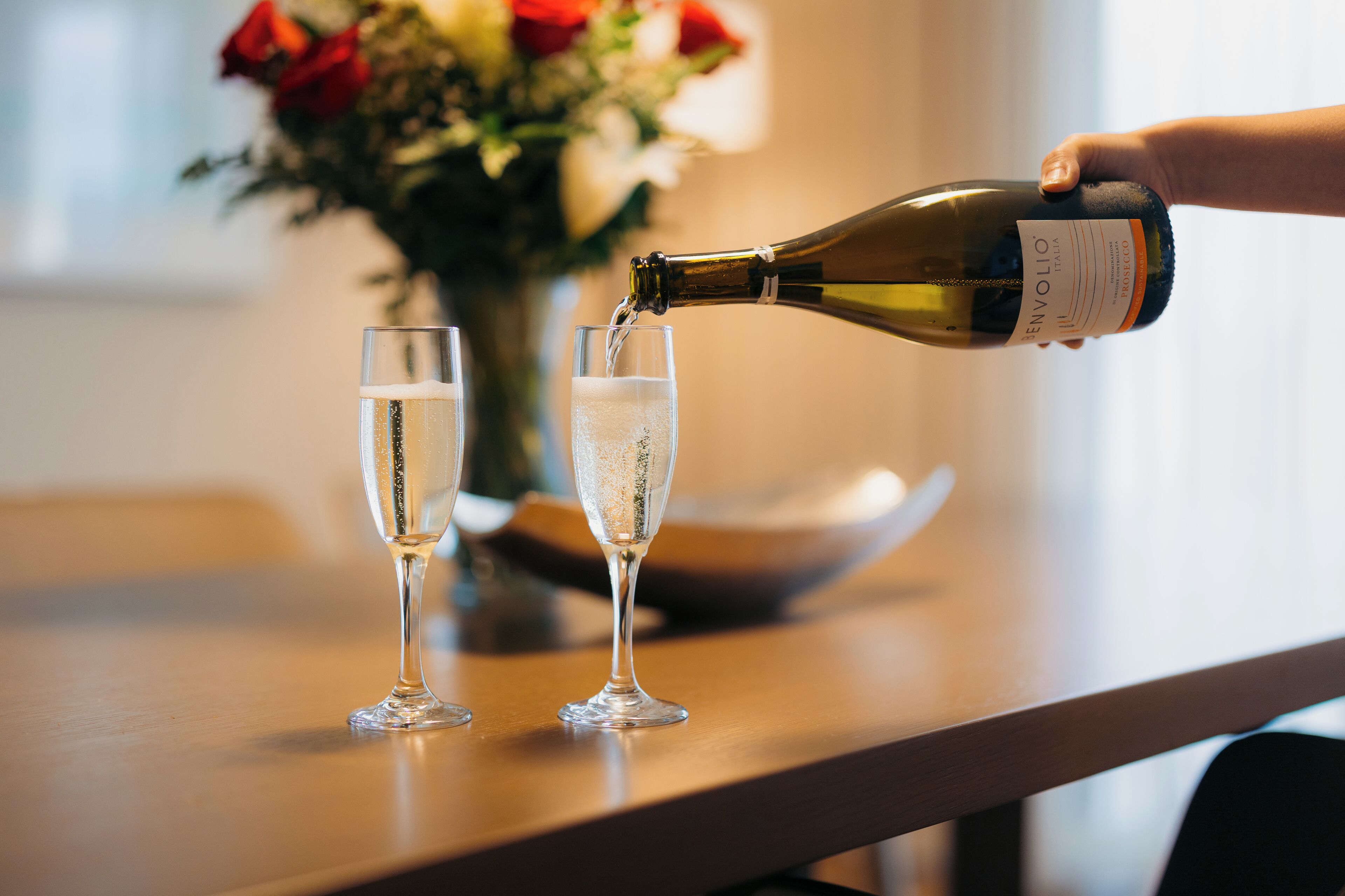 A bottle of wine being poured into two glasses on a table.