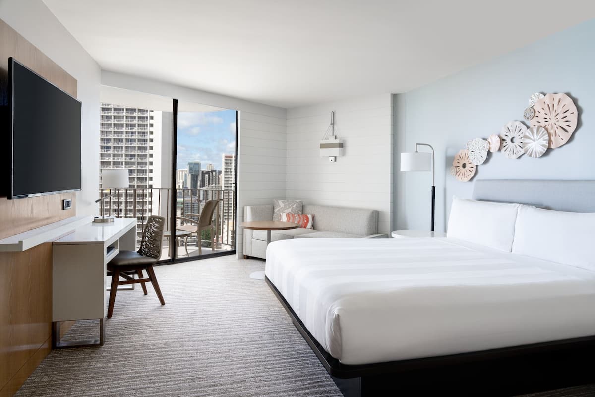 Ein modernes Hotelzimmer mit einem großen Bett, einem Schreibtisch, einem Stuhl, einem kleinen Tisch und einem Fernseher.