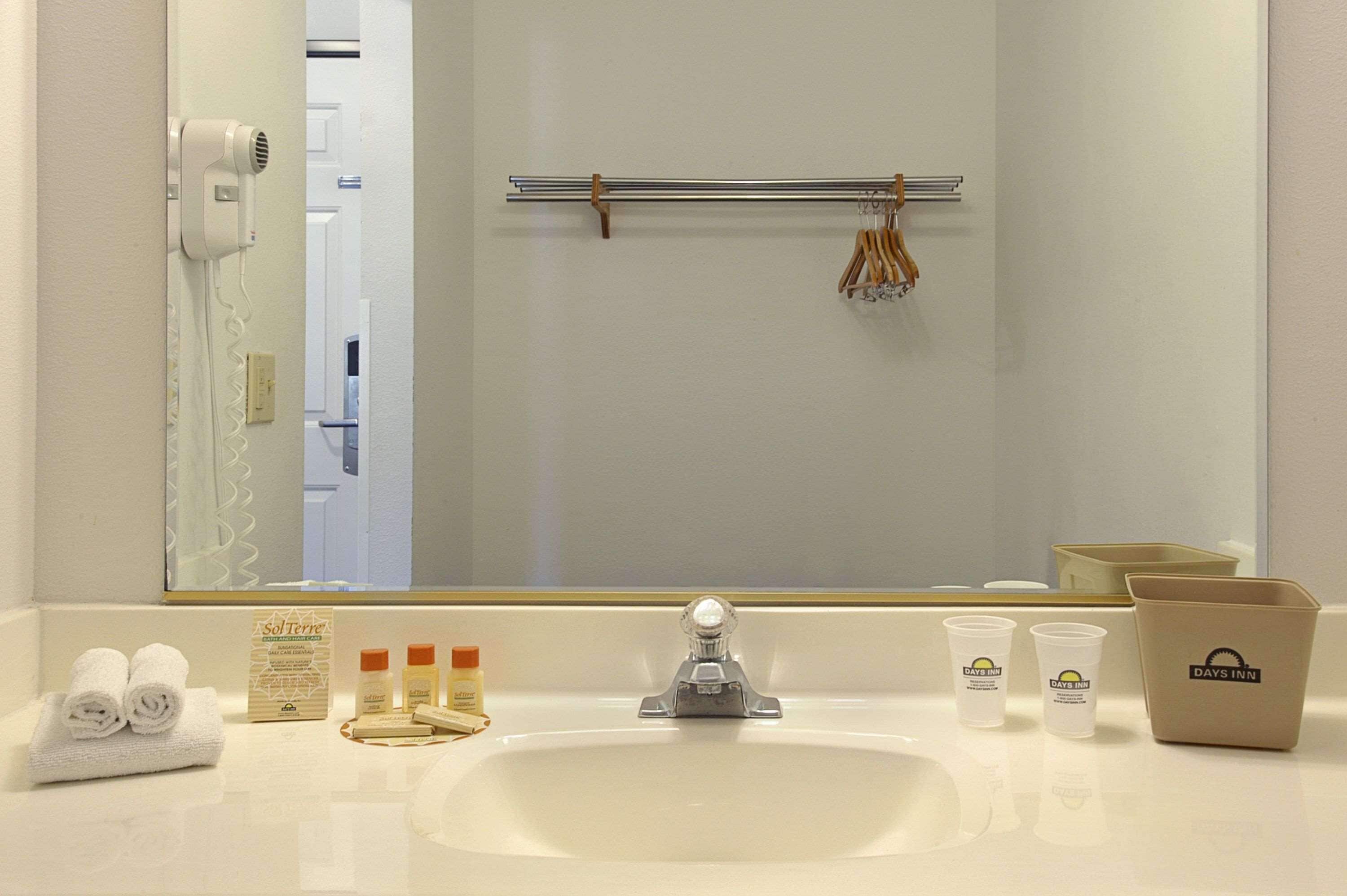 A hotel bathroom with a sink, mirror, towel rack, and toiletries.