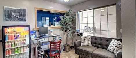 A compact living space with a kitchenette, a sofa, a desk with a computer, and a refrigerator stocked with beverages.