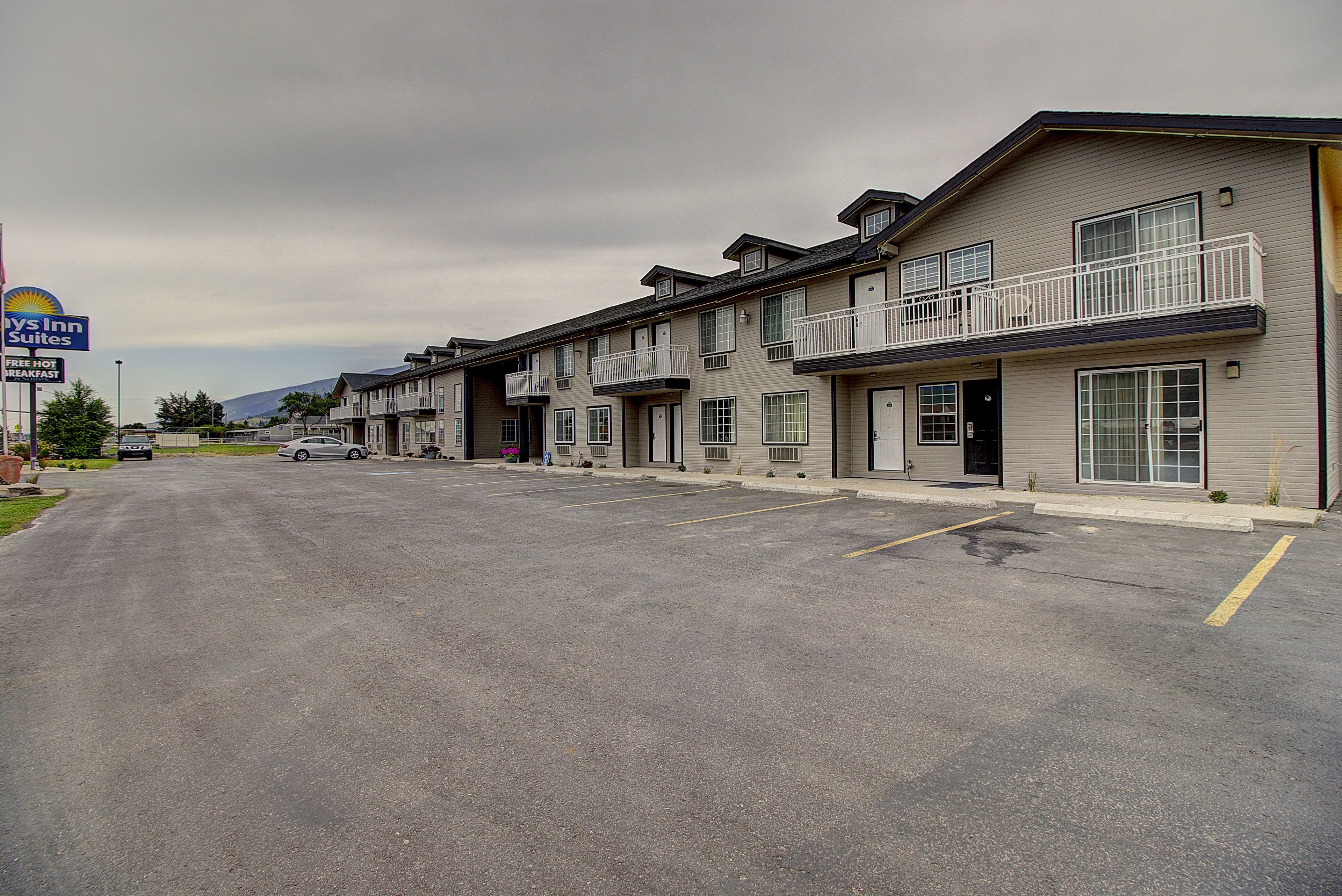 A row of motel buildings with balconies and a parking lot in front.