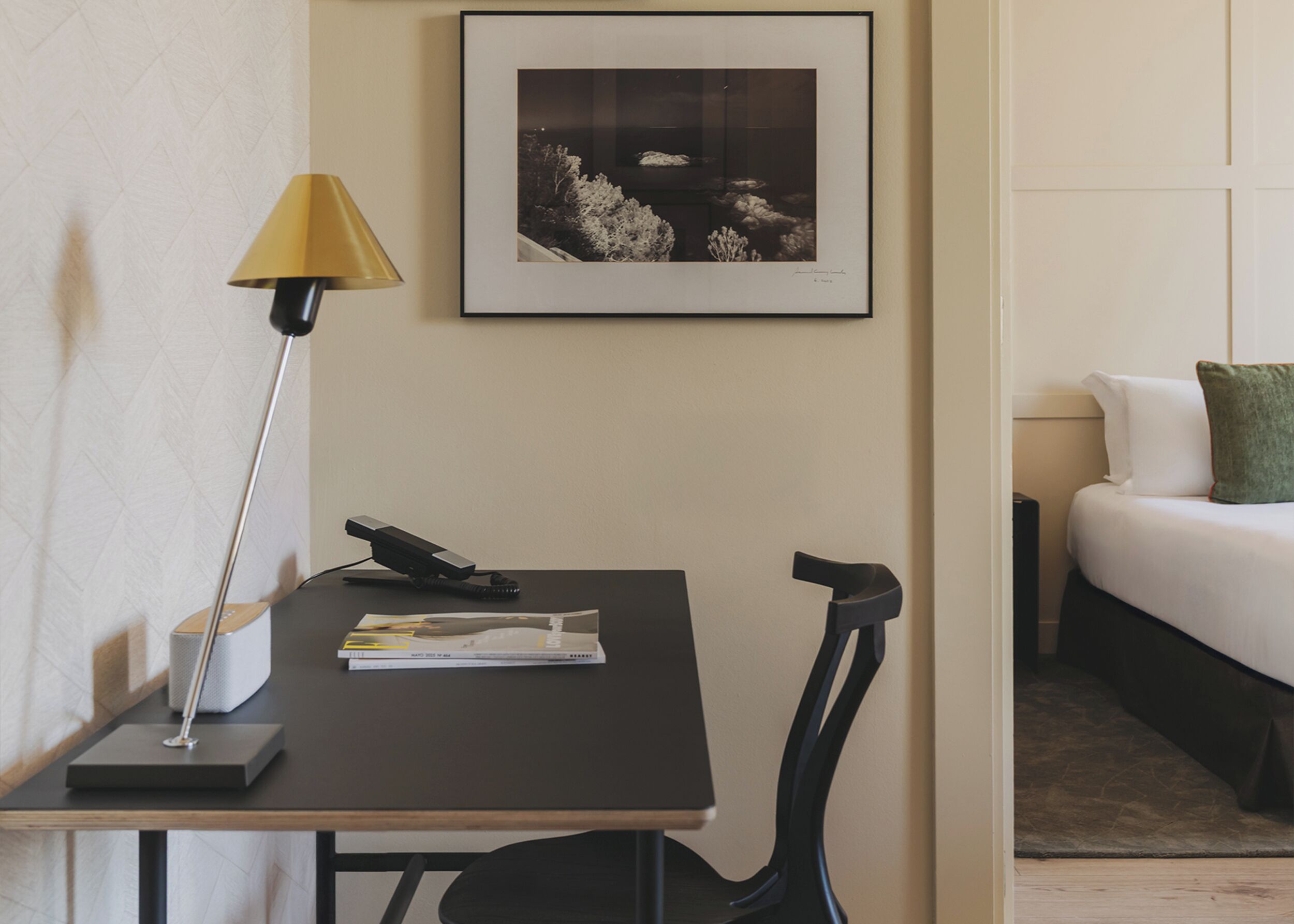 Habitación de hotel con escritorio, lámpara, un cuadro enmarco, cama con almohadas y piso alfombrado.