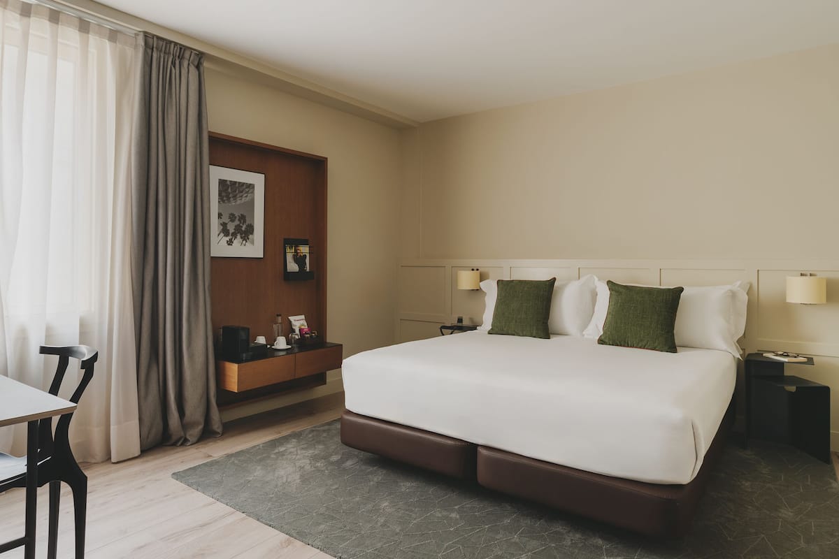 A hotel room with a large bed, a desk, a chair, a nightstand, and a small table.
