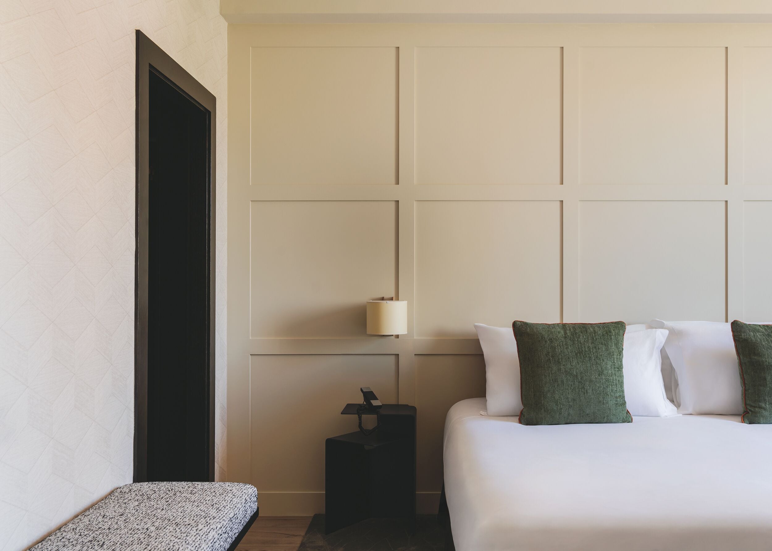 Una habitación de hotel con una cama, una mesita de noche, una lámpara y un banco.