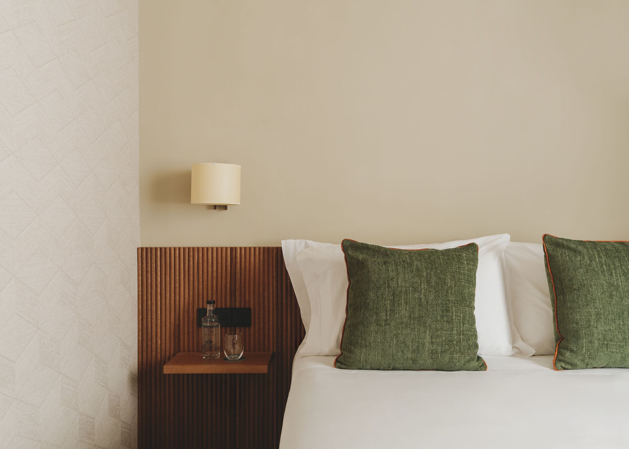Une chambre d’hôtel avec un lit, une table de chevet, une lampe et une bouteille.