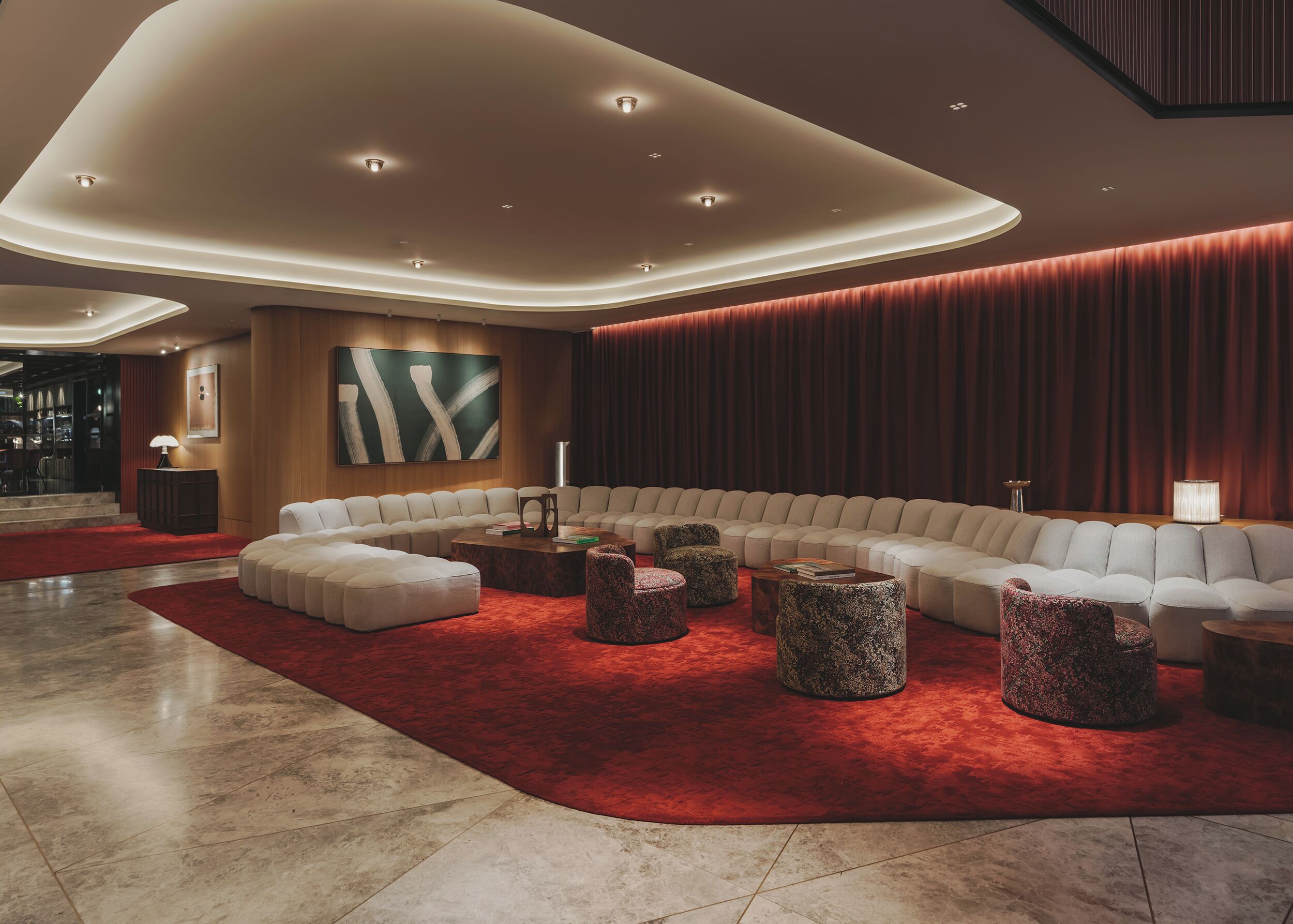 A modern living room with a curved sectional sofa, multiple ottomans, and a red carpet.