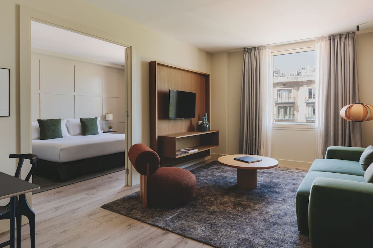 A modern hotel room with a bed, a sofa, a TV, and a view of the city.