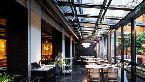 Un restaurante con techo de vidrio, mesas, sillas y plantas en macetas.