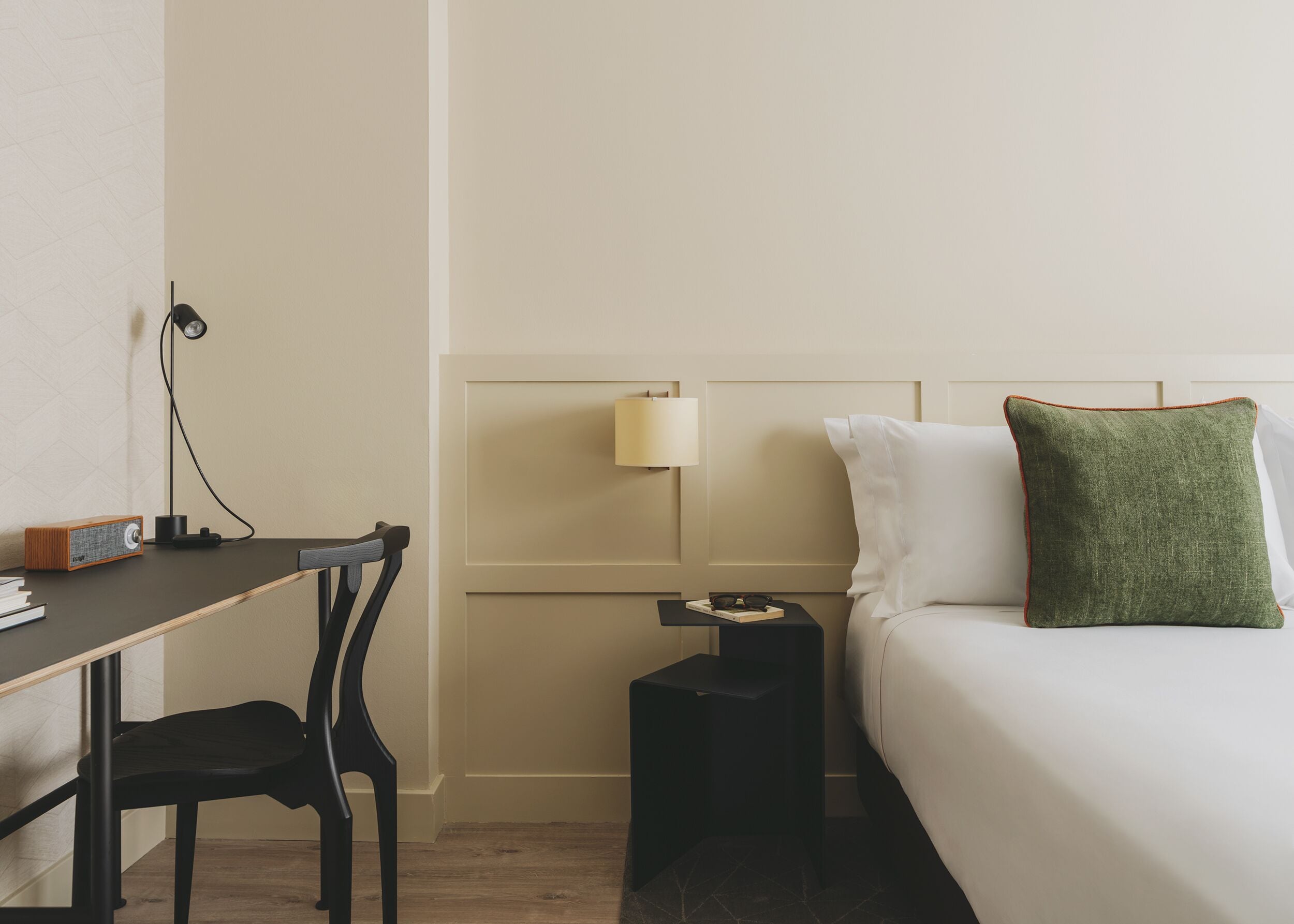 Una habitación de hotel con cama, escritorio, silla, mesita de noche y lámpara.