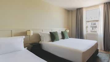 Habitación de hotel con dos camas, una mesita de noche, una lámpara y una ventana con cortinas.