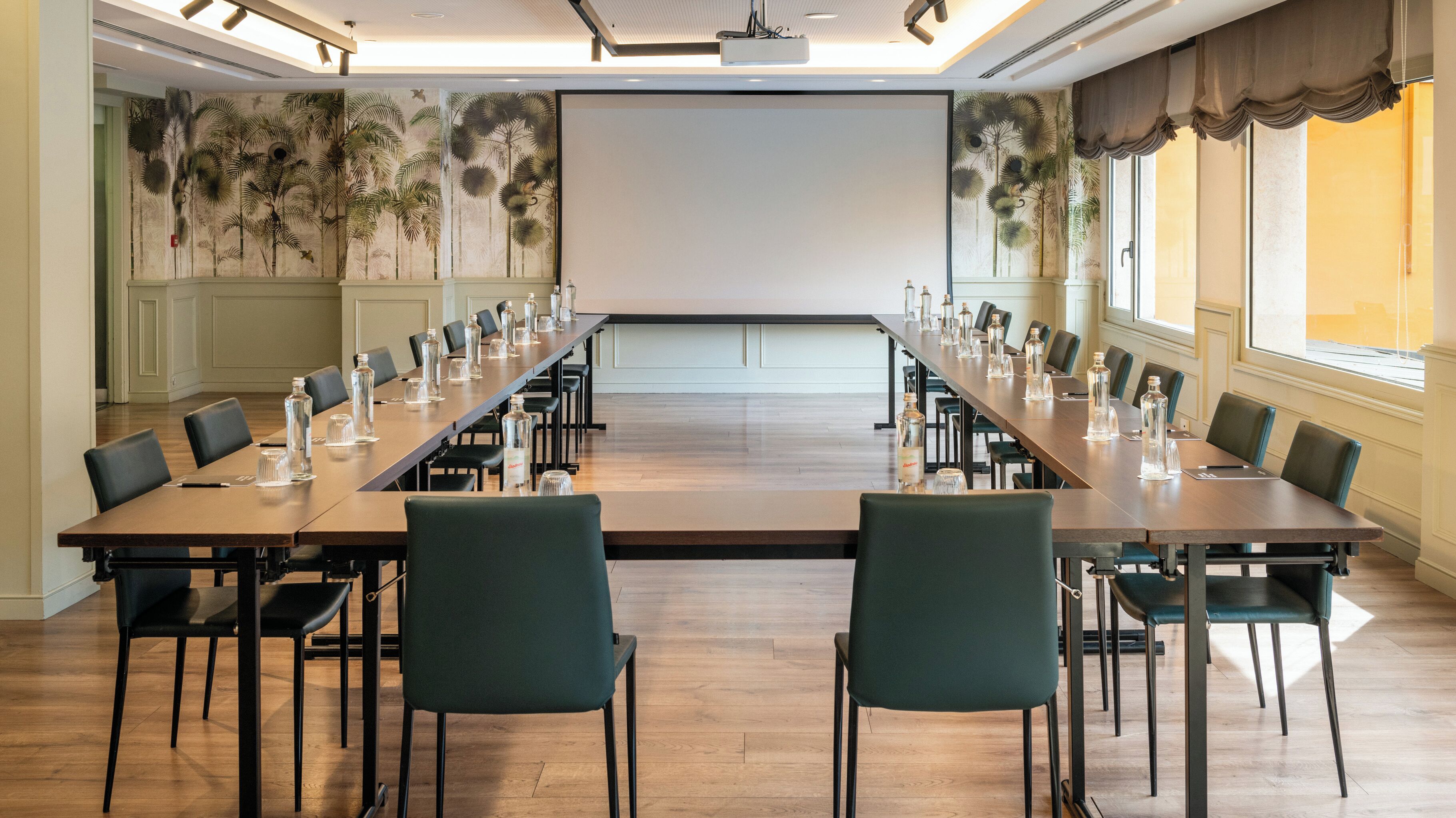 Ein Konferenzraum mit einem langen Tisch, Stühlen und einer Projektionsleinwand.