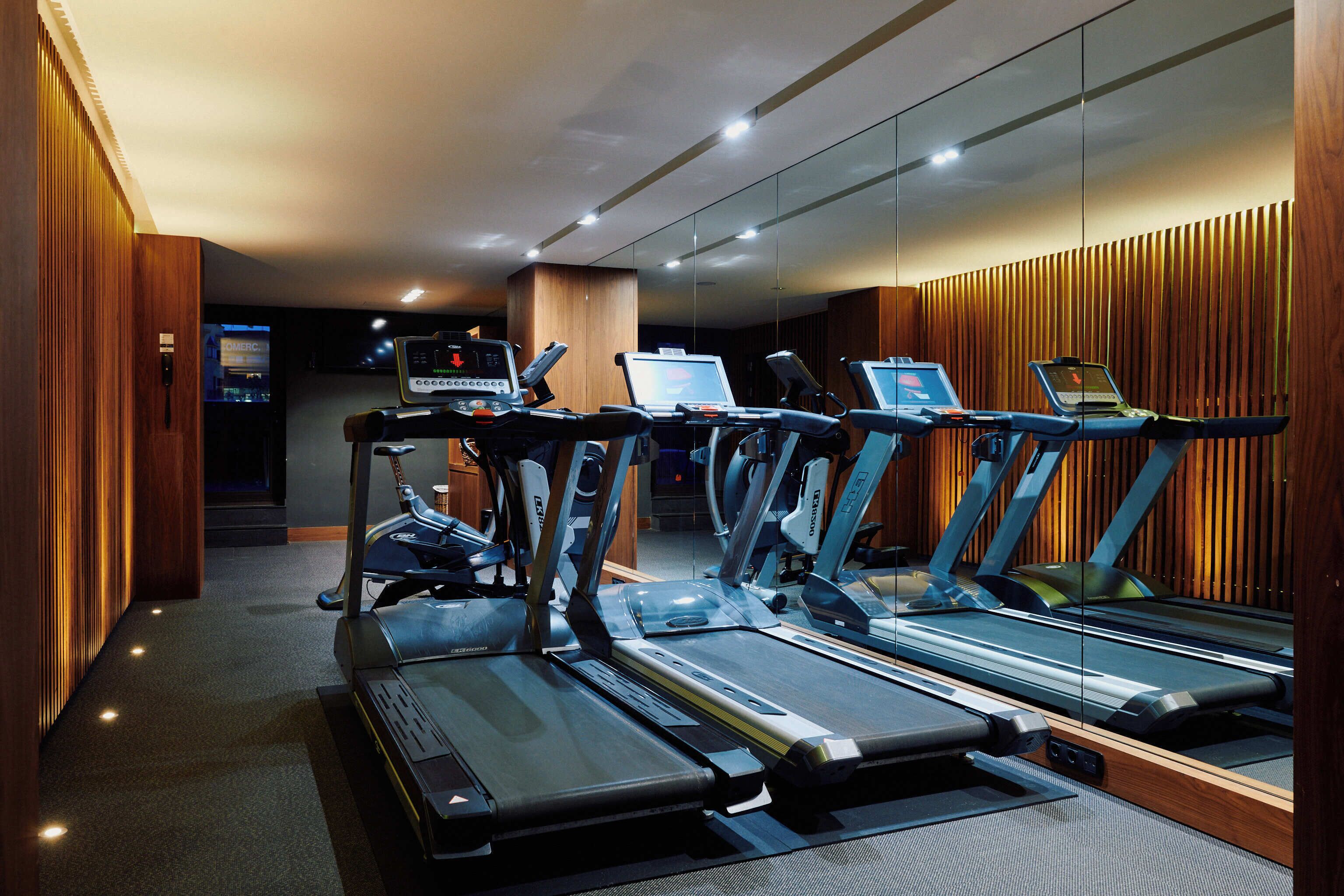 Un gimnasio con cintas de correr, bicicletas estáticas y un ordenador portátil sobre un escritorio.