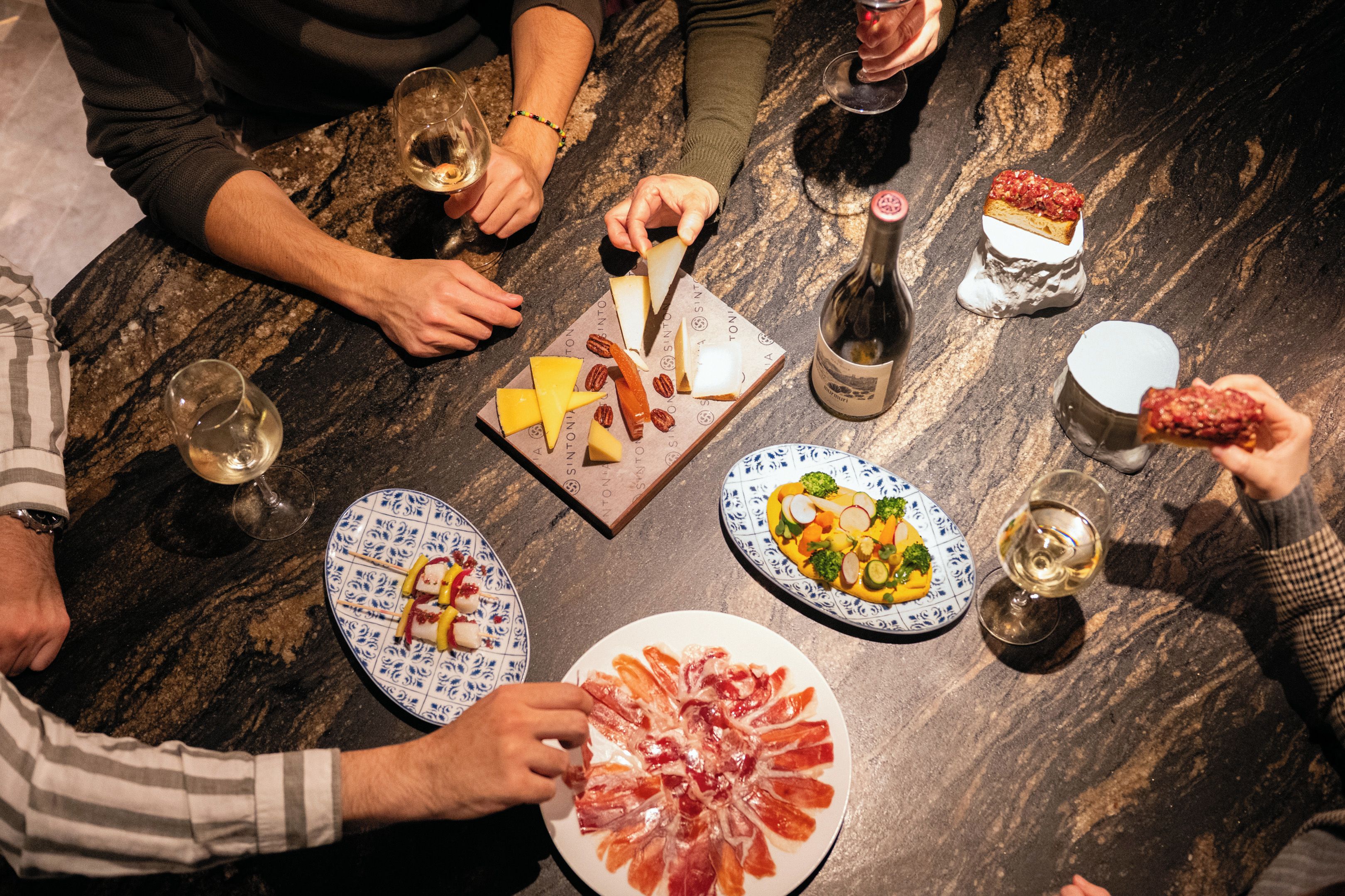 A group of people seated around a marble table with various food items and drinks.