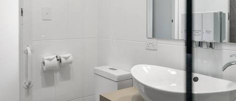 Et moderne badeværelse med hvid vask, toilet og bruseområde.