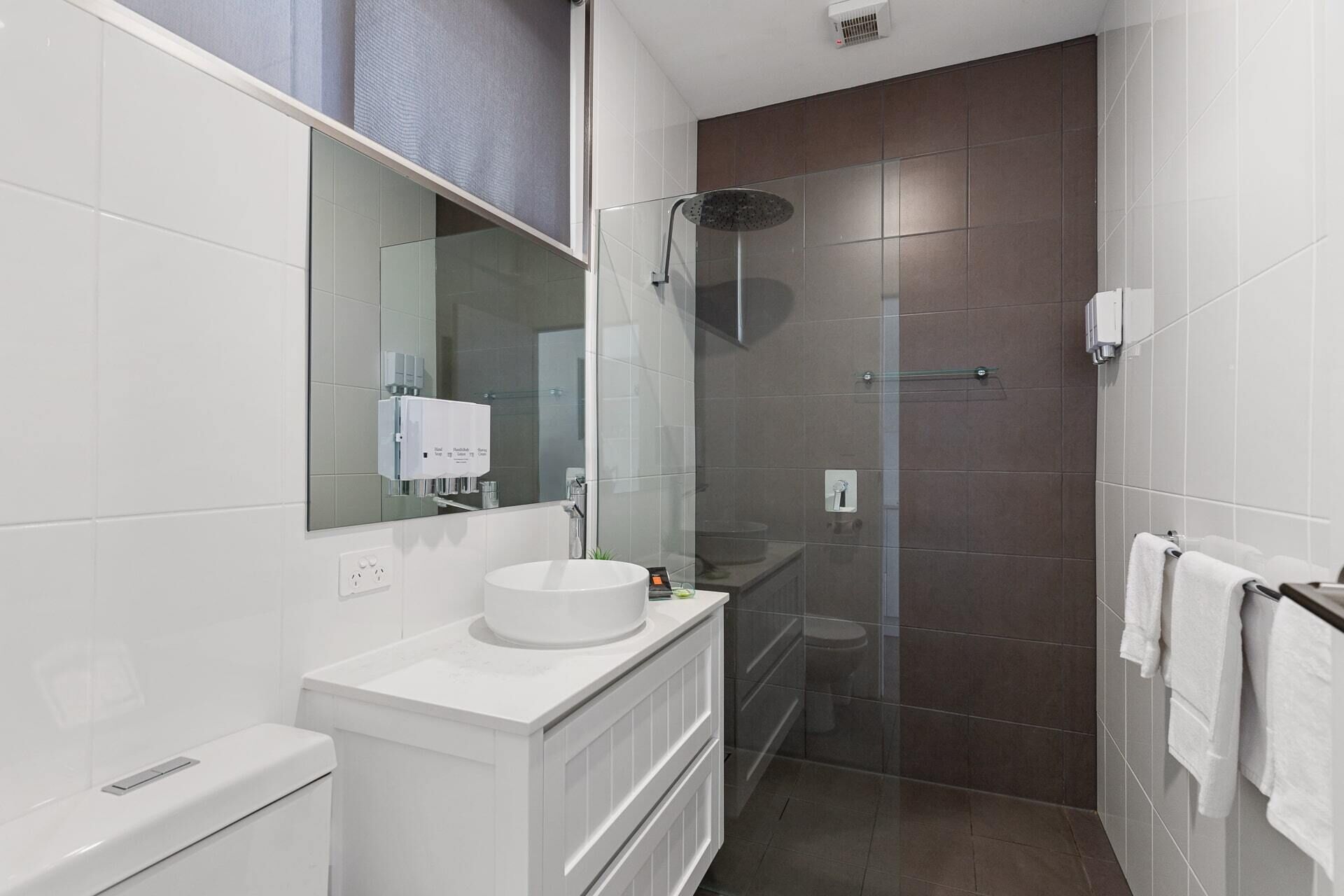 A modern bathroom with a white vanity, a glass shower enclosure, and a large mirror.