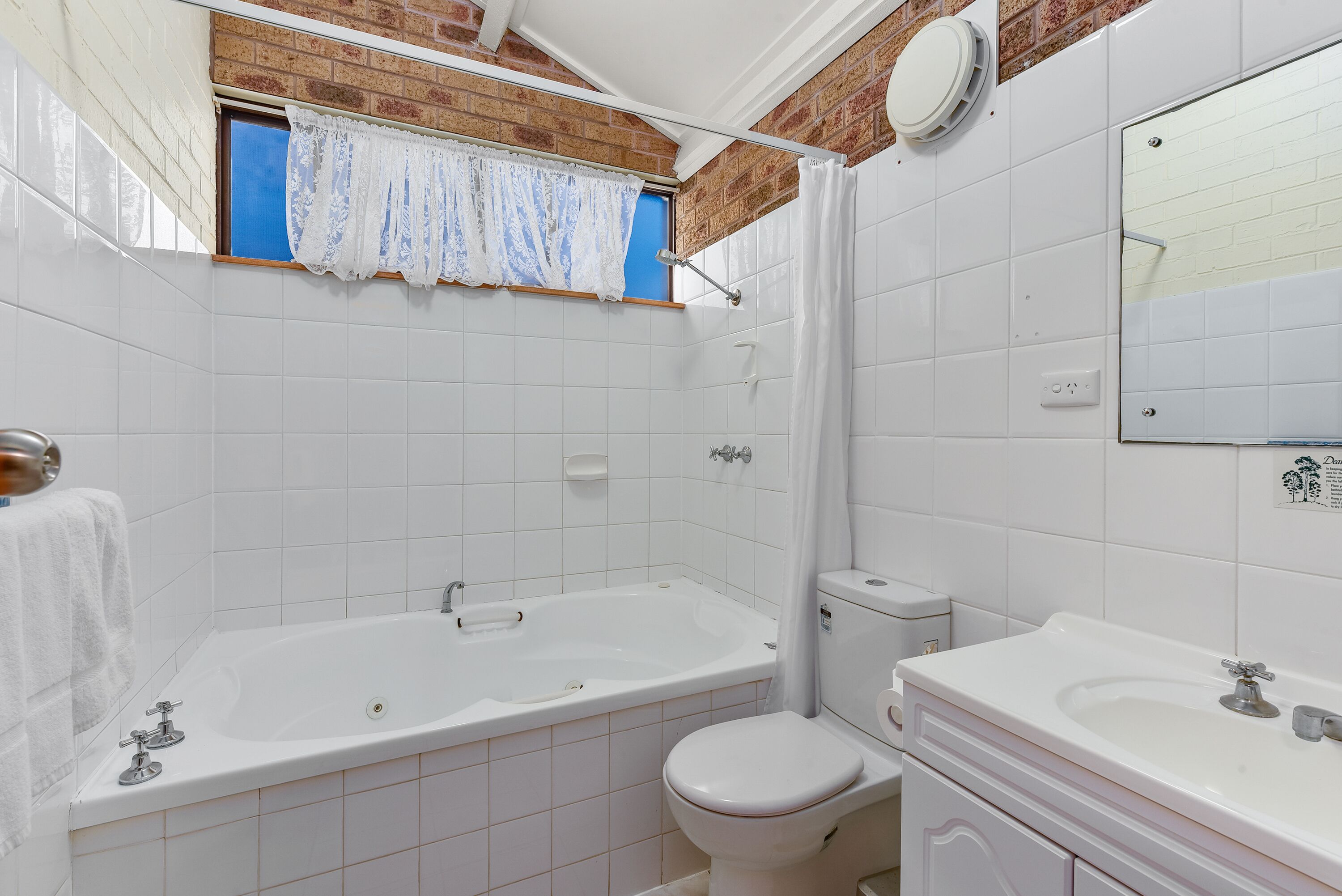 A bathroom with a bathtub, toilet, and sink, featuring white tiles and a brick accent wall.