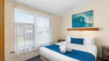 Una habitación de hotel con una cama, un cuadro de una ola y una ventana con cortinas translúcidas.