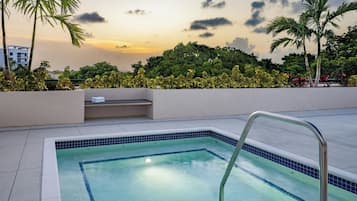 Una piscina con una escalera metálica, rodeada por un muro bajo y abundante vegetación.