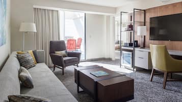 Habitación de hotel con sofá, sillones, una mesa de centro, televisor y escritorio con lámpara.