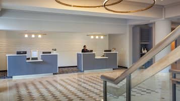 A hotel reception area with two reception desks, a patterned floor, and a staircase.