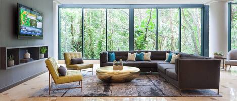 A modern living room with a large sectional sofa, a round coffee table, and a flat-screen TV mounted on the wall.