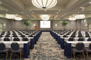 Un salón de conferencias con filas de mesas y sillas, una pantalla grande al frente e iluminación decorativa.