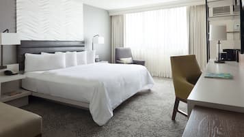 Habitación de hotel con una cama grande, un escritorio, una silla, una lámpara y una ventana con cortinas.