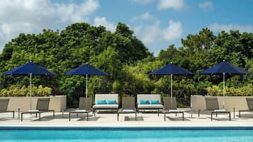 A poolside area with lounge chairs and umbrellas, surrounded by lush greenery.