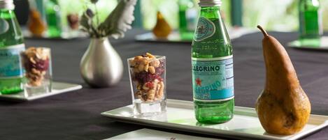 Una mesa con una botella de agua, un vaso con frutos secos y fruta tallada sobre un plato blanco.