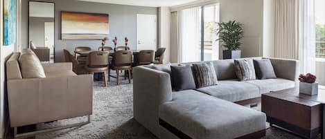 A modern living room with a sofa, armchairs, a coffee table, and a dining area with chairs and a table.