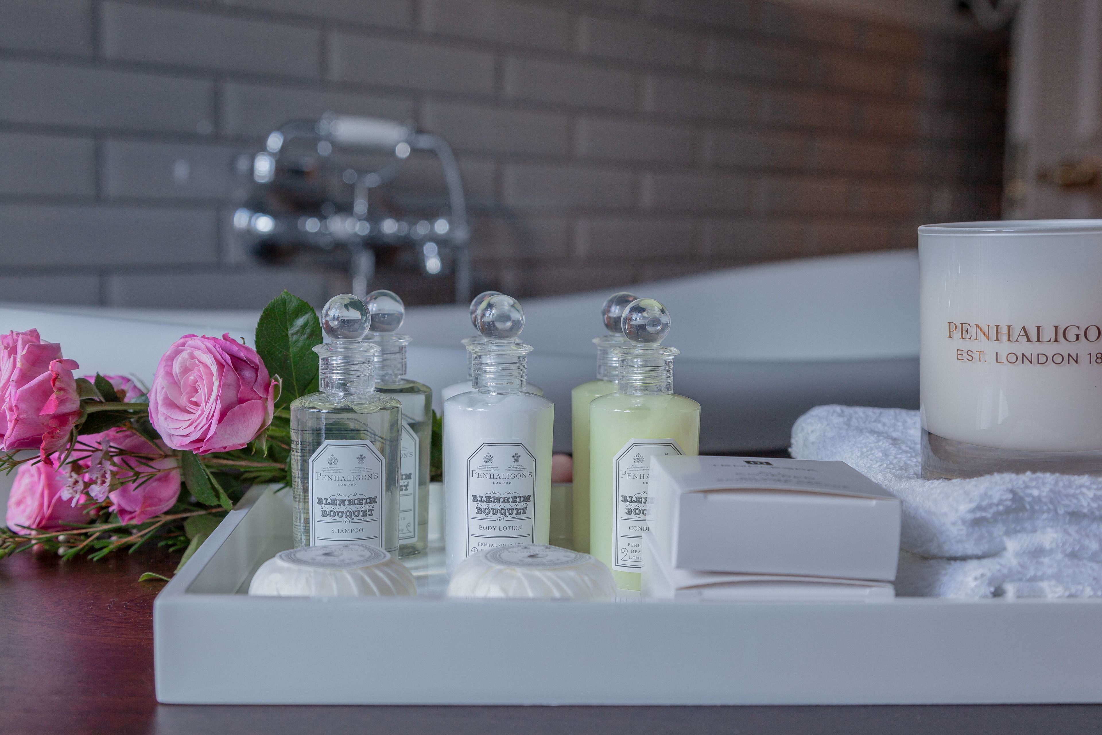 Um lavatório de casa de banho com produtos de higiene pessoal, incluindo um frasco de champô, loção corporal e uma vela.