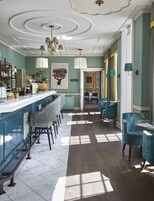 A bar area with a long counter, multiple stools, and a chandelier. There are chairs and a table in the adjacent seating area.