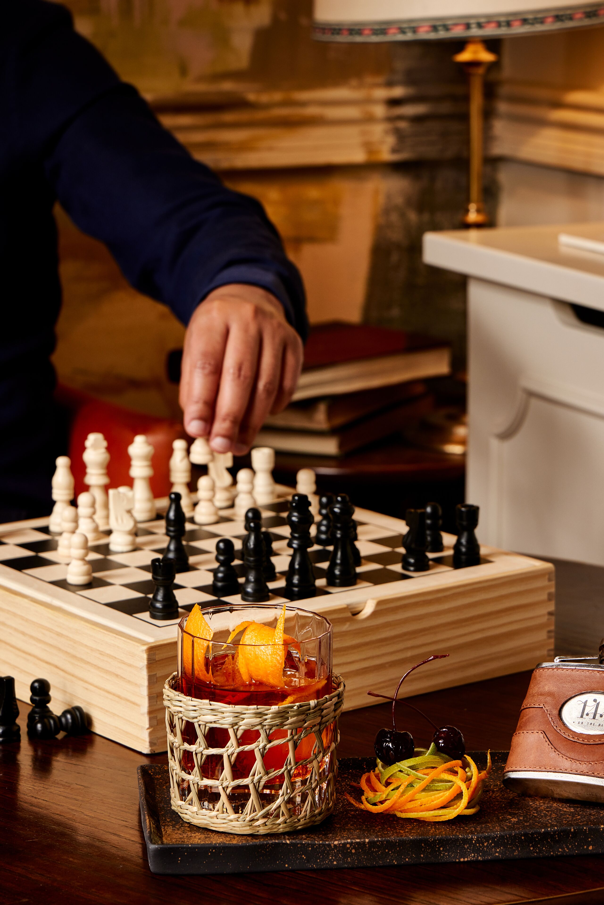 A chessboard with pieces, a glass of drink, and a clock on a table.