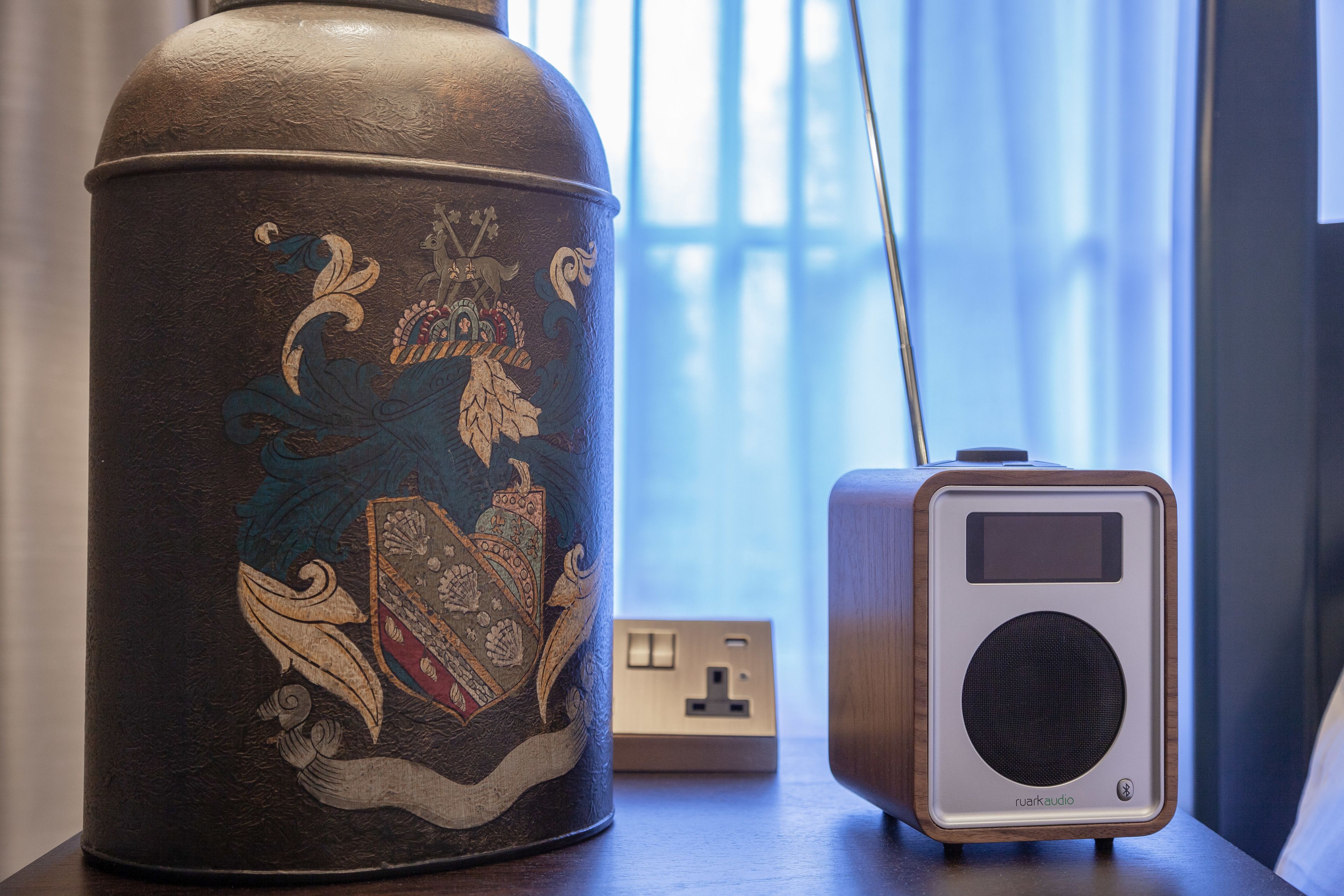 A decorative urn with intricate designs next to a modern speaker on a wooden table.